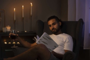 Мужчина сидит в кресле с книгой и бокалом